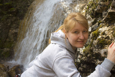 Portrait of smiling woman standing against waterfall