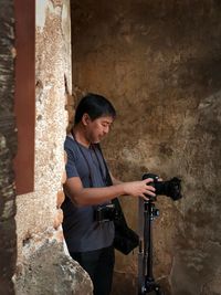 Side view of young man photographing against wall
