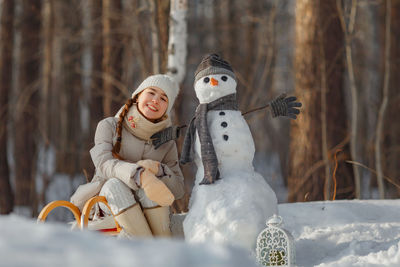 Portrait of teenage girl with snowman in forest