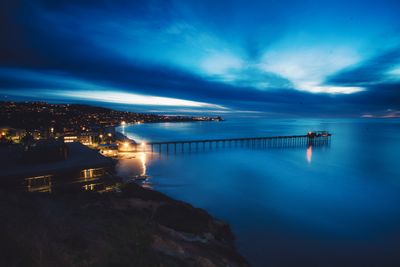 Illuminated bridge over river against sky at night