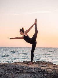 Full length of woman doing yoga at beach against sky during sunset