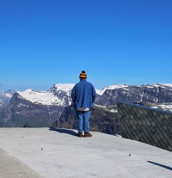 Rear view of man standing on mountain against clear blue sky