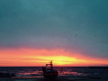 Silhouette birds flying over sea against sky during sunset