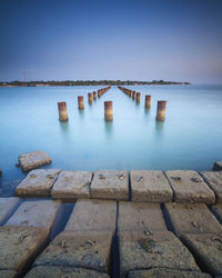 Wooden posts in sea against clear blue sky