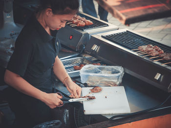 Side view of woman preparing food on barbecue grill