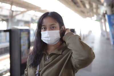 Portrait of beautiful young woman wearing mask on railroad station platform