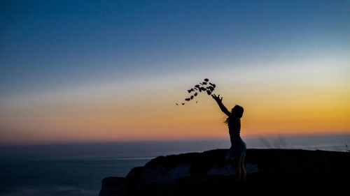 Silhouette of woman throwing leaves against sky during sunset