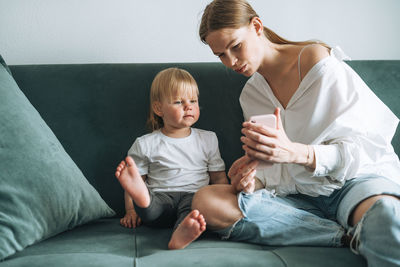 Young mother and cute baby girl using mobile phone at home