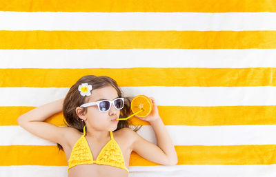 Girl sipping juice from orange fruit through straw lying on towel