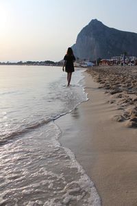 Rear view of woman walking on shore at beach against sky