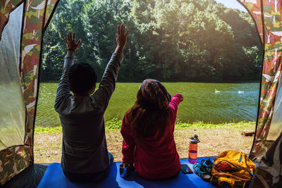 Rear view of people sitting on mat by lake