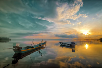 Fishing boat moored in sea against sky during sunset