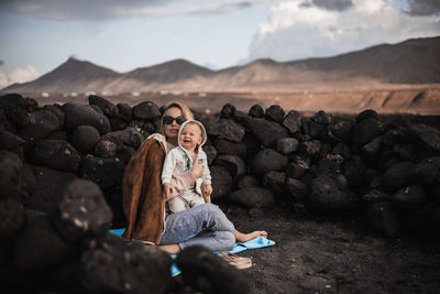 Mother enjoying winter vacations playing with his infant baby boy son on black sandy volcanic beach