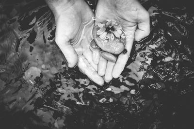 Cropped hands holding pebbles in lake
