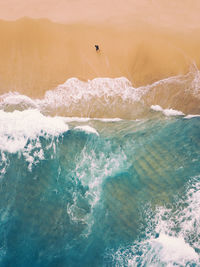 Aerial view of a lone man walking on a sandy beach full of waves 