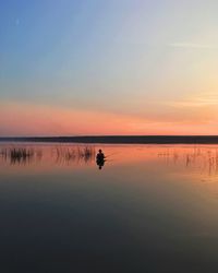 Scenic view of sea with man fishing against sky during sunset