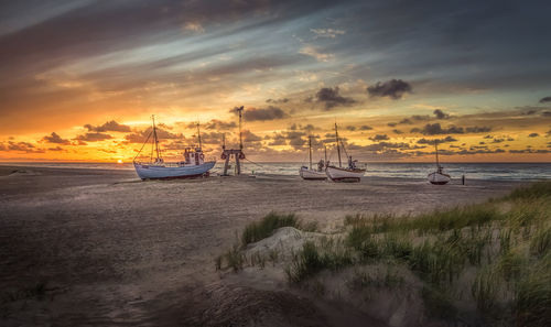 Boats moored on beach against sky during sunset