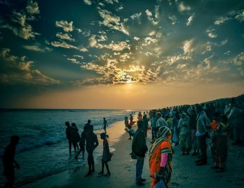 People walking on beach against sky during sunset