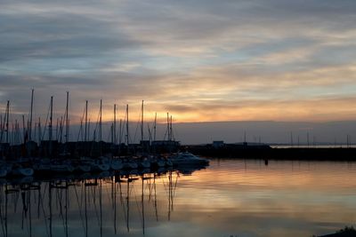 Sailboats moored in harbor at sunset