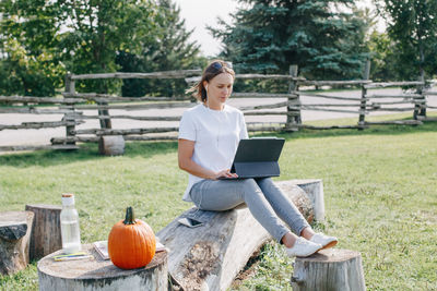 Full length of smiling woman using laptop while sitting at park