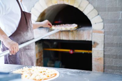 Midsection of chef preparing pizza in restaurant kitchen