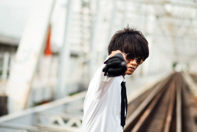 Portrait of young man gesturing while standing on railroad track 