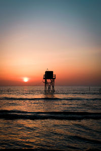 Silhouette hut on sea against sky during sunset