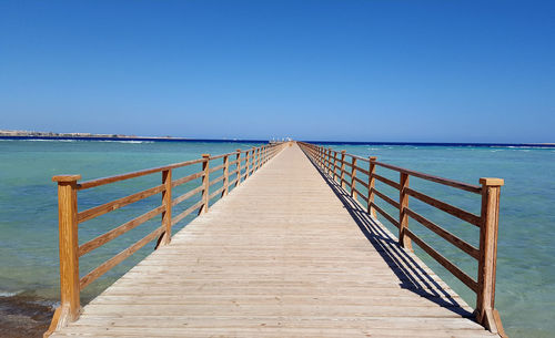 Pier over sea against clear blue sky