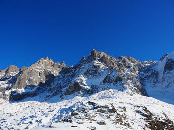 Low angle view of snowcapped mountains against clear blue sky