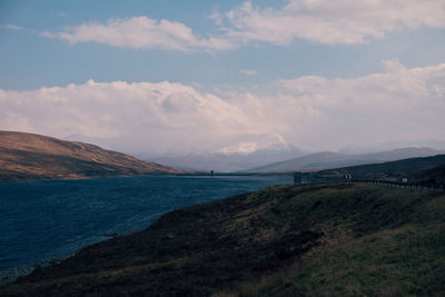 Large body of water surrounded by hills and a partially cloudy sky