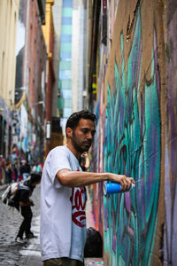 Side view of young man standing against wall in city