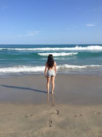 Rear view of woman standing at beach against sky