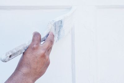 Cropped hand of person painting white wall