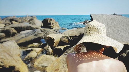 Rear view of woman wearing sun hat at rocky shore