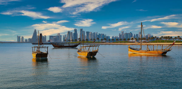 Doha skyline from the corniche promenade in afternoon showing dhows with qatar flag in arabic gulf 