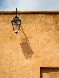 Low angle view of electric lamp hanging against sky