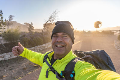 Male hiker takes a selfie with the sun rising from behind.