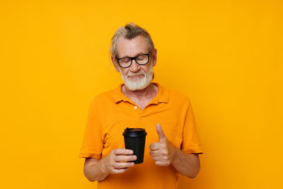 Portrait of senior woman holding trophy against yellow background