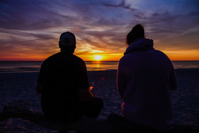 Rear view of silhouette couple looking at sea during sunset