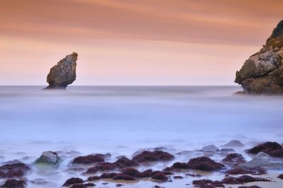 Rocks in sea against sky during sunset