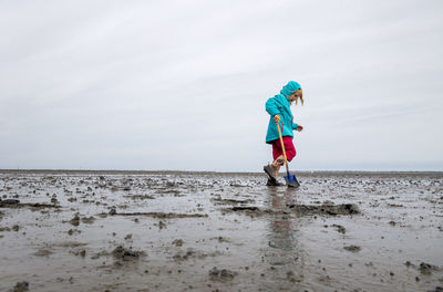 Girl playing in mud flat against sky at lower saxon wadden sea national park, germany