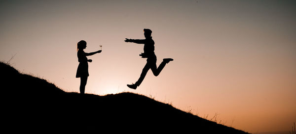 Silhouette man with woman jumping against clear sky during sunset
