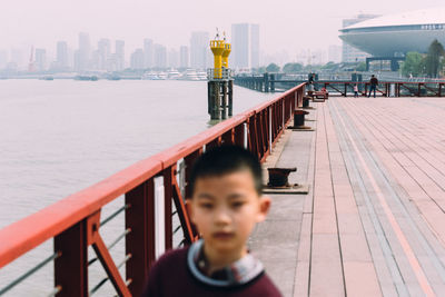 Boy standing by railing in city against sky