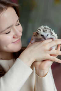 Girl holds cute hedgehog in her hands. portrait of pretty curious muzzle of animal. favorite pets. 