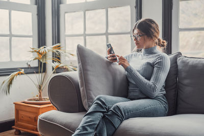 Young woman using phone while sitting on sofa at home