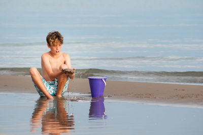 Boy playing in water at beach against sky