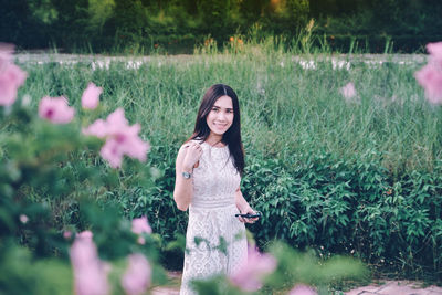 Portrait of smiling woman standing by flowering plants