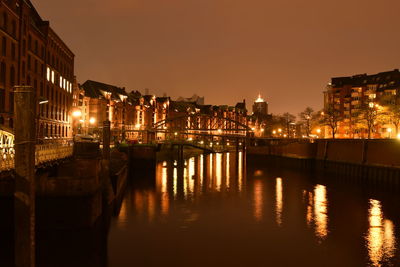 Illuminated city by river against clear sky at night