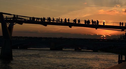 Silhouette bridge over river in city against sky during sunset