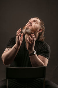 Young man sitting against black background